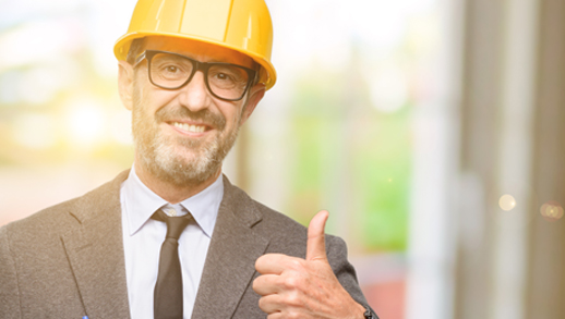 This image shows a man doing a thumbs-up sign. He is wearing a yellow hard hat.