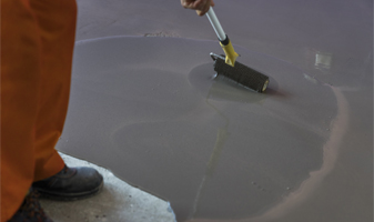 This image shows a man painting an industrial floor using a paint roller.