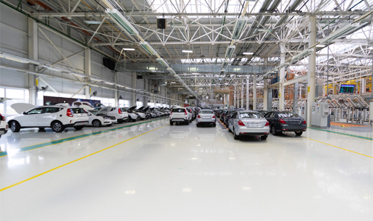This image shows a car plant whit a white epoxy floor. There a re a lot of cars.