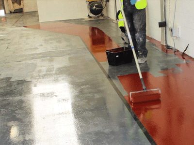 The image shows a man painting a floor using a roller brush.