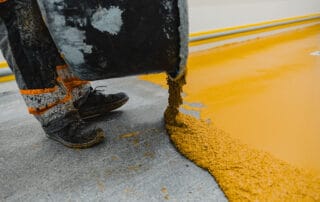 This image shows a man pouring yellow epoxy paint on a bare floor.